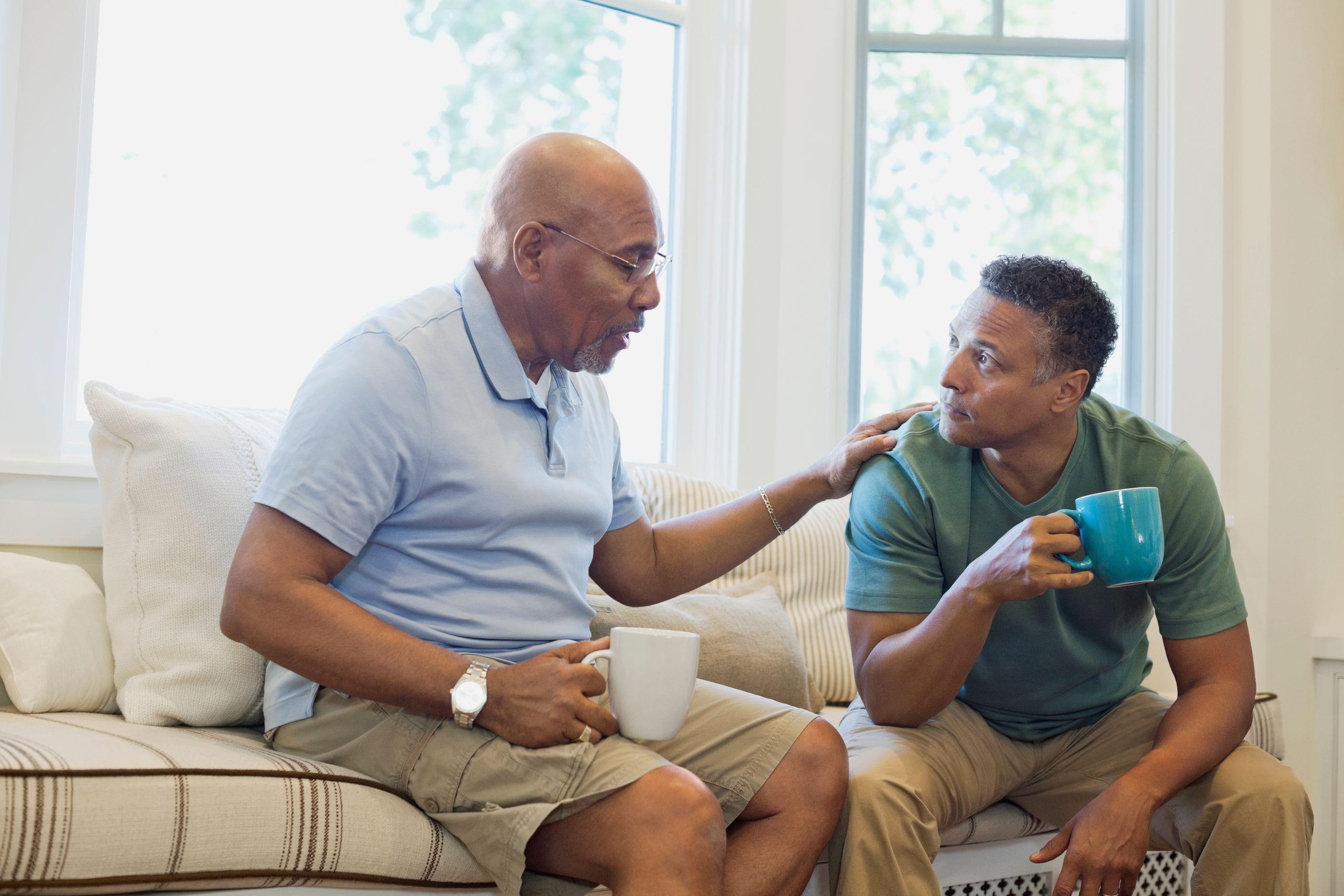 Senior father and son talking while having coffee on sofa.